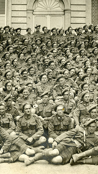 Photographie de groupe en noir et blanc d’une douzaine de soldats vêtus de leur uniforme de Highlanders, y compris des kilts. Les hommes sont photographiés sur les marches d’un château français.