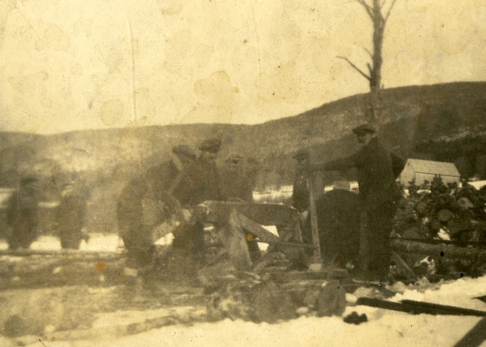 Photographie sépia d’hommes en train de couper du bois en hiver dans un paysage rural.